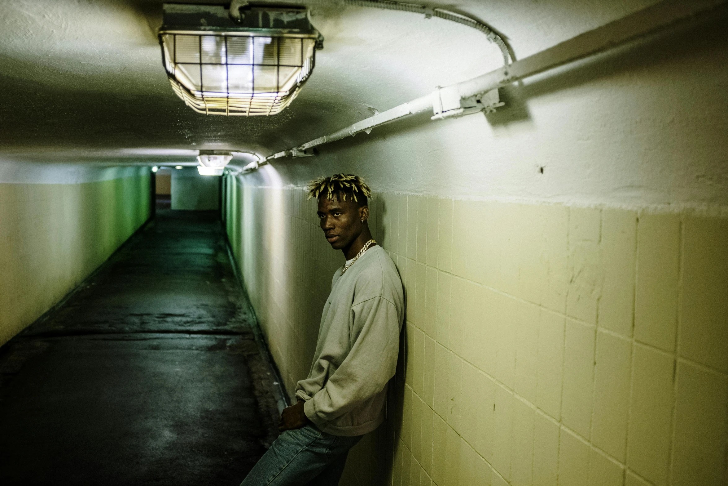 a man leaning against a wall in a tunnel, an album cover, inspired by Gordon Parks, unsplash contest winner, hyperrealism, xxxtentacion, blonde man, wiz khalifa, in an underground parking garage