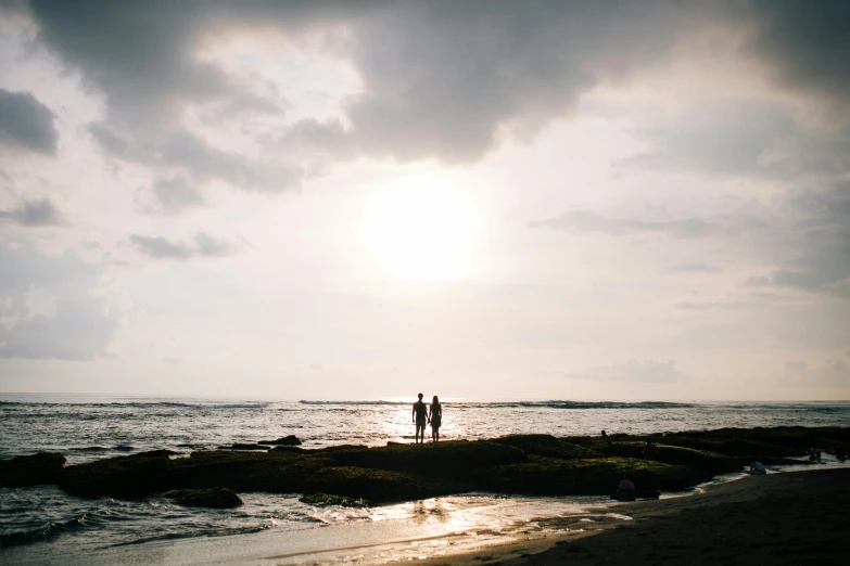 a couple of people standing on top of a sandy beach, unsplash, bali, light coming through, instagram photo, distant photo