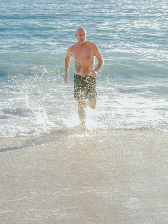 a man running out of the water on a beach, no hair completely bald, promo image, fan favorite, jony ive