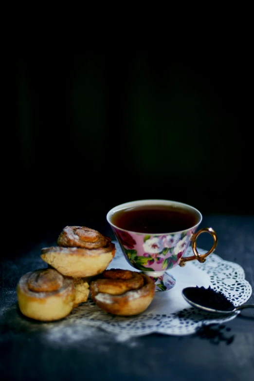 a cup of tea and some pastries on a table, inspired by Wlodzimierz Tetmajer, dark bacgkground, victoria, te pae, photoshoot