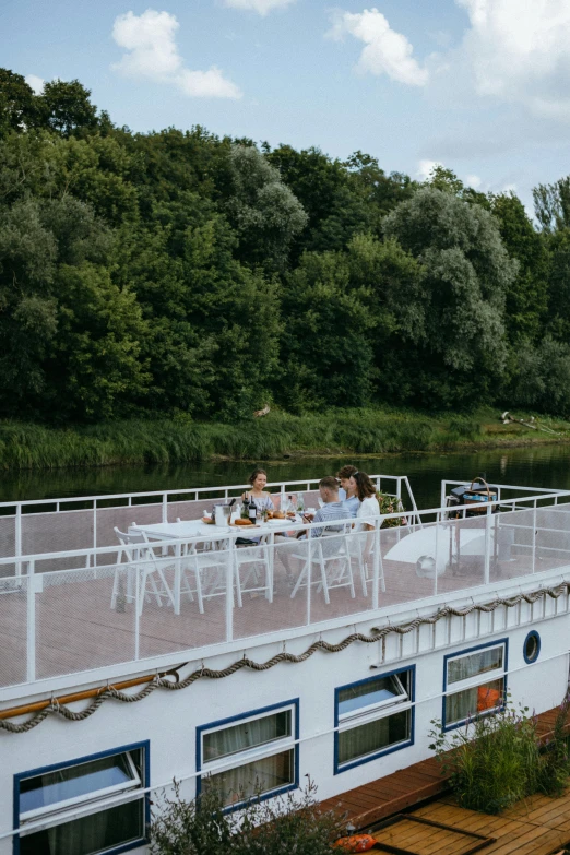 a group of people sitting on top of a boat, restaurant, near a river