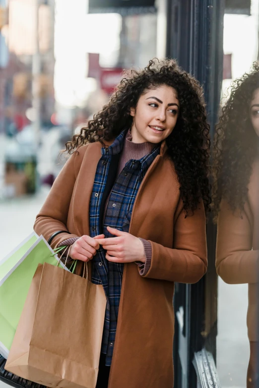 a woman standing in front of a store window holding shopping bags, pexels contest winner, renaissance, brown curly hair, light brown coat, young middle eastern woman, promotional image