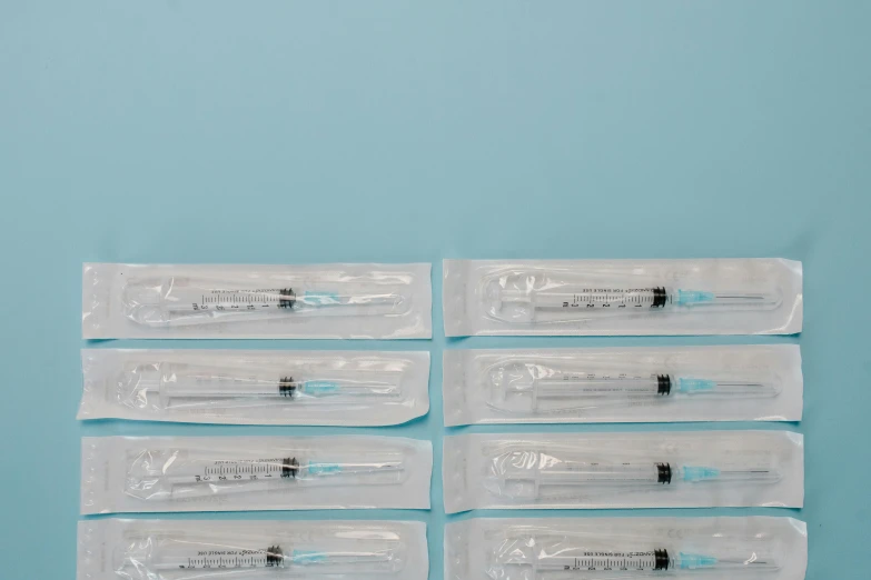 a bunch of syops sitting on top of a blue surface, an album cover, by Matija Jama, pexels, holding syringe, surgical iv bag, lined up horizontally, on a pale background