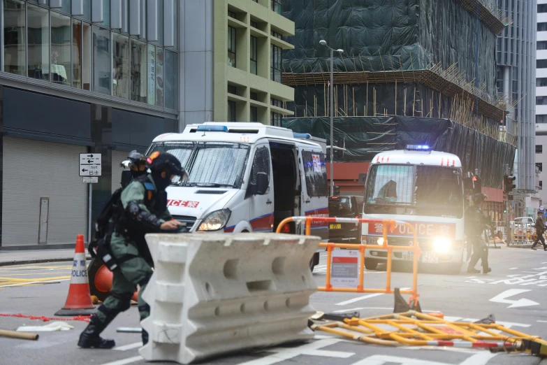 a group of police officers standing on the side of a road, by Joseph Severn, shutterstock, hurufiyya, street of hong kong, collapsed buildings, view from a news truck, square