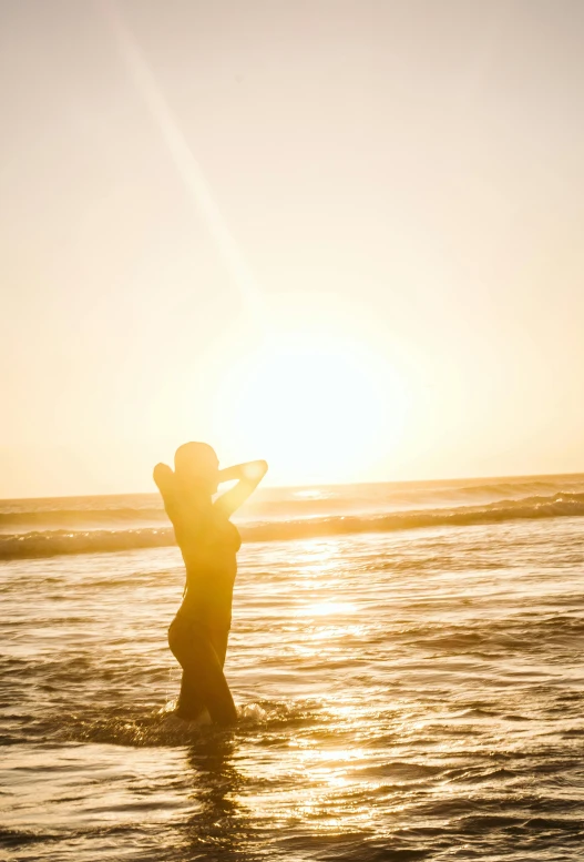 a woman standing in the ocean at sunset, bright sunny time, golden hour”