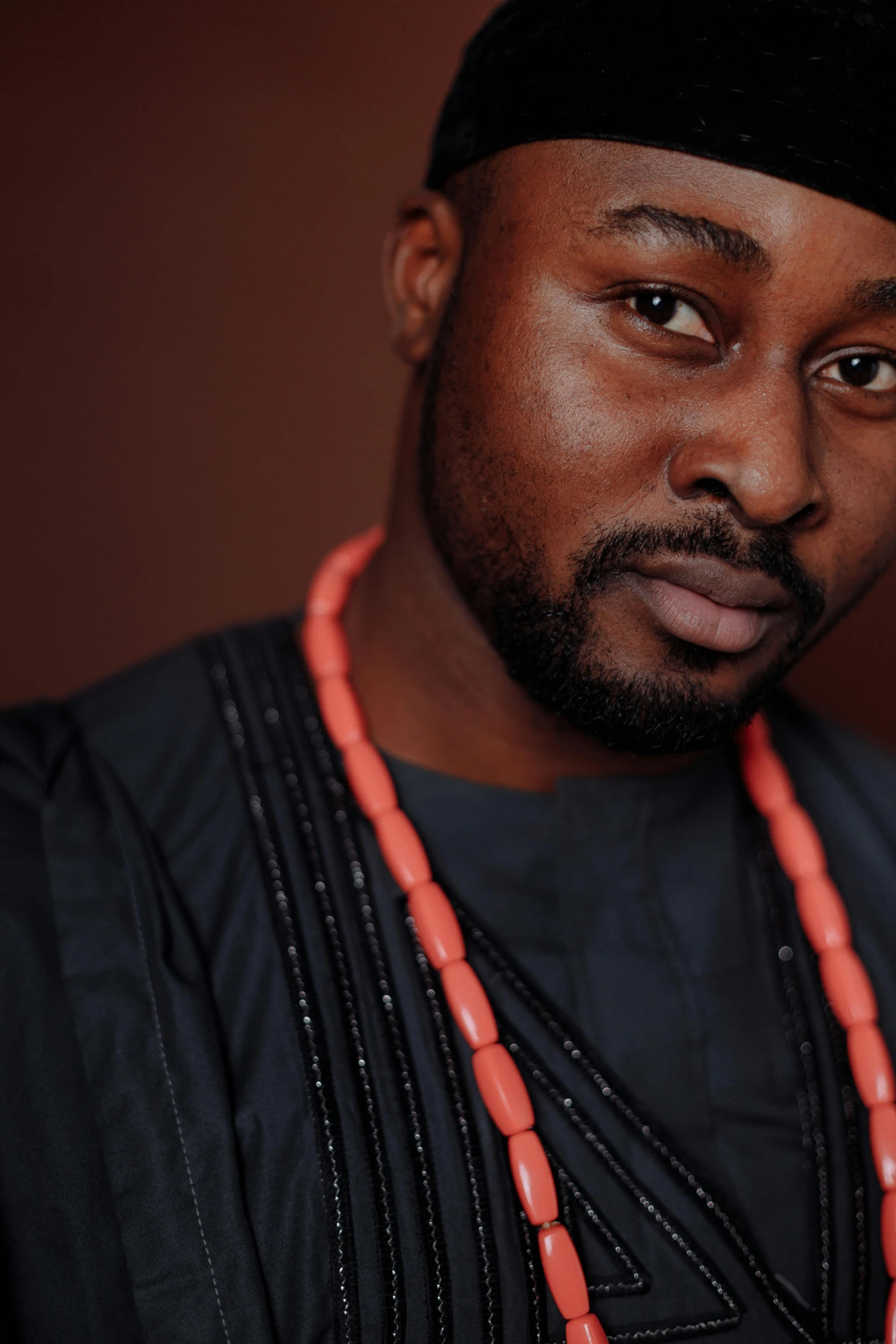 a man in a black shirt and a red beaded necklace, inspired by Ras Akyem, backdrop, wearing an african dress, ikenobo, softly lit