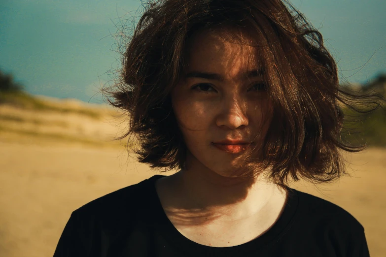a woman standing on top of a sandy beach, inspired by Tang Yifen, pexels contest winner, shin hanga, big cheekbones, messy bob, malaysian, soft shadows on the face