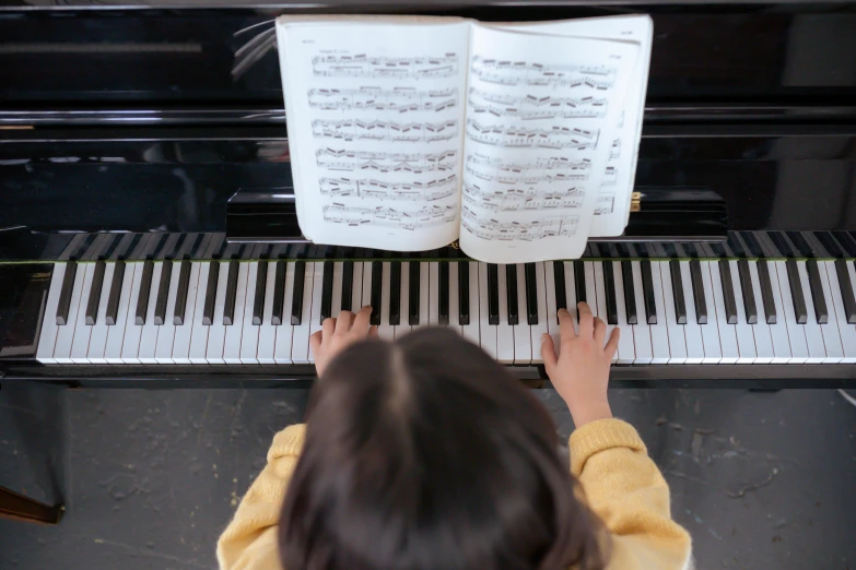 a little girl that is playing a piano, an album cover, pexels, birdseye view, student, sheet music, black