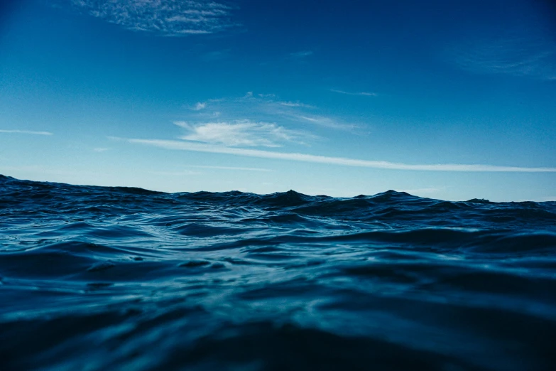 a large body of water under a blue sky, an album cover, unsplash, wavy water, navy, depths, concerned