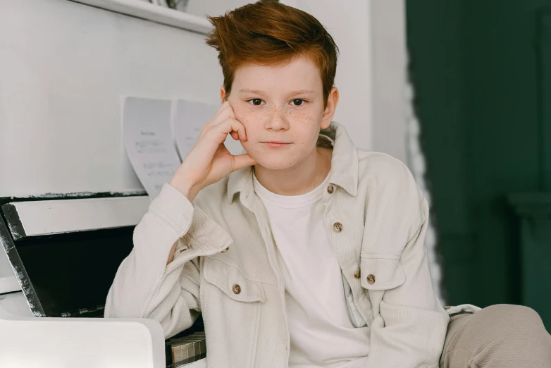 a young boy sitting on top of a piano, by Emma Andijewska, trending on pexels, realism, ginger hair with freckles, on a white table, wearing jacket, headshot profile picture