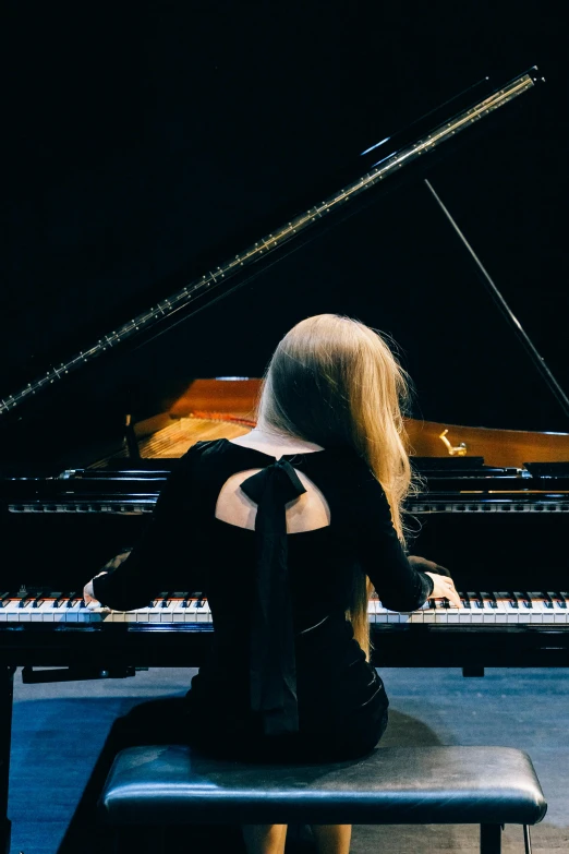 a woman sitting on a bench in front of a piano, inspired by Louisa Matthíasdóttir, unsplash, performing on stage, from back, blonde, profile image