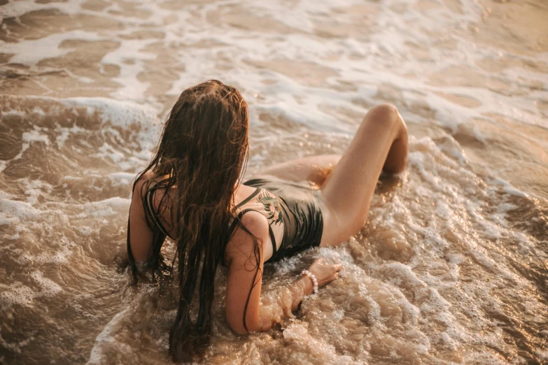 a woman laying on top of a beach next to the ocean, inspired by Elsa Bleda, pexels contest winner, wet flowing hair, attractive body, profile image, brown water