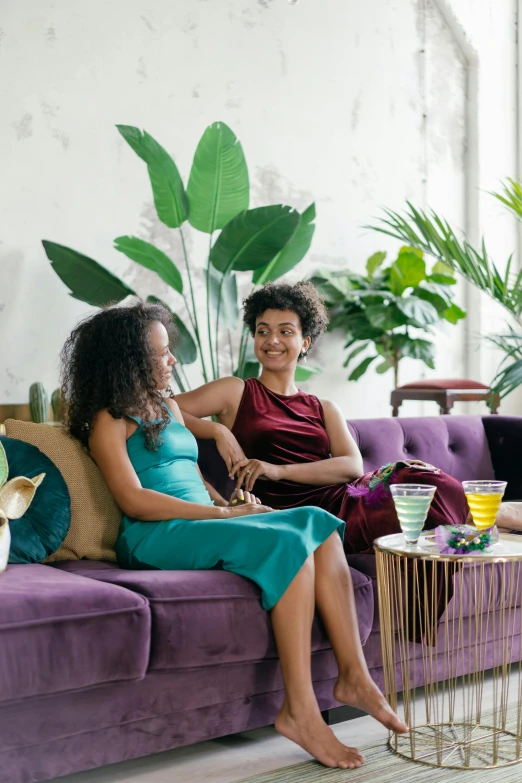 two women sitting on a purple couch in a living room, featured on pinterest, tropical houseplants, with afro, emerald color palette, customers