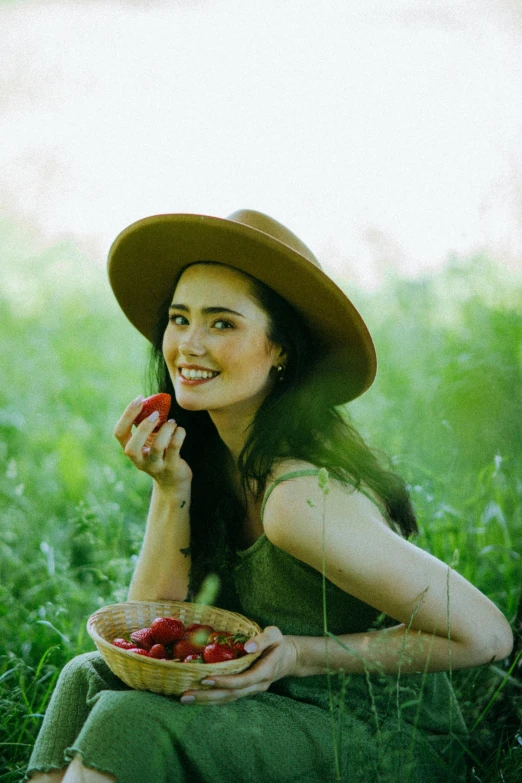 a woman sitting in the grass holding a bowl of strawberries, pexels contest winner, lily collins, with hat, mai anh tran, red apples