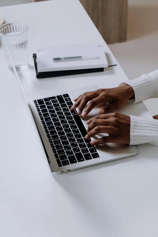 a woman sitting at a desk typing on a laptop, by Carey Morris, trending on unsplash, wearing a white sweater, black on white, afro tech, hands straight down