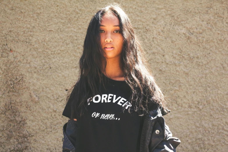 a woman with long hair standing in front of a wall, an album cover, by Robbie Trevino, tumblr, outlive streetwear collection, library of forever, black teenage girl, wearing a black!! t - shirt
