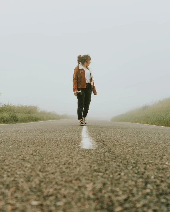 a person walking down a road on a foggy day, an album cover, by Hannah Tompkins, pexels contest winner, happening, queer woman, panoramic view of girl, wearing white sneakers, looking off into the distance