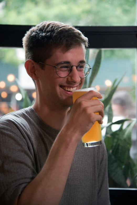 a man sitting at a table with a glass of beer, by Washington Allston, trending on reddit, cute slightly nerdy smile, large glasses, hazy, ignant