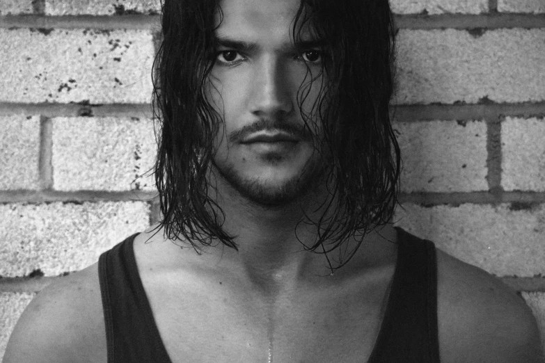 a man with long hair standing in front of a brick wall, a black and white photo, inspired by Jorge Jacinto, flickr, beautiful face!!!!, john snow, sweaty face, black hair and brown eyes