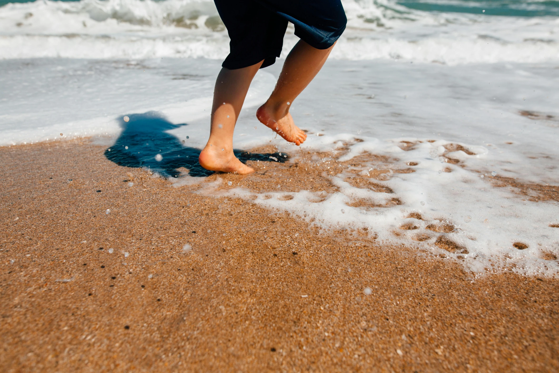 a person standing on a beach next to the ocean, wet feet in water, kids playing at the beach, profile image