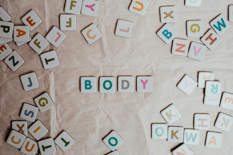 a table topped with lots of wooden letters, a mosaic, by Emma Andijewska, pexels contest winner, letterism, {perfect body}, fluffy body, bubblegum body, white body