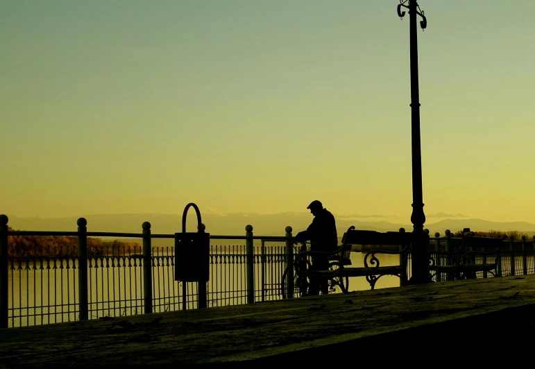 a person riding a bike next to a body of water, inspired by George Pirie, pexels contest winner, romanticism, benches, silhouette :7, old man, spring evening