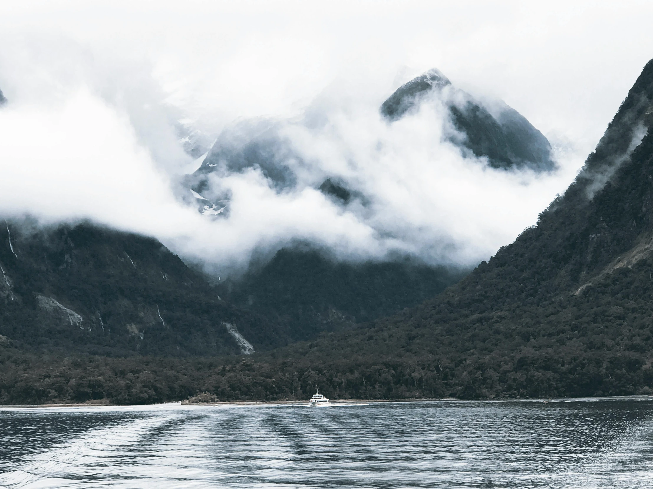 a boat in a body of water with mountains in the background, inspired by Pierre Pellegrini, pexels contest winner, white steam on the side, te pae, lachlan bailey, gray clouds