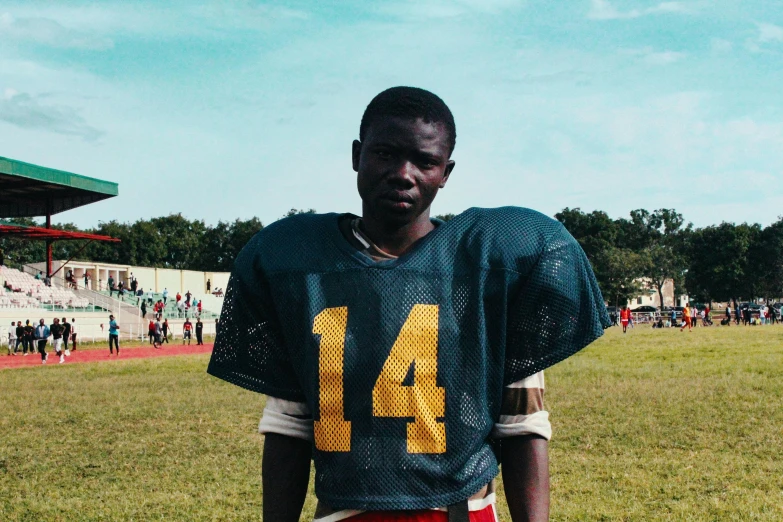 a man in a football uniform standing on a field, by Daniel Lieske, hurufiyya, black teenage boy, indie film, adebanji alade, award winning movie still