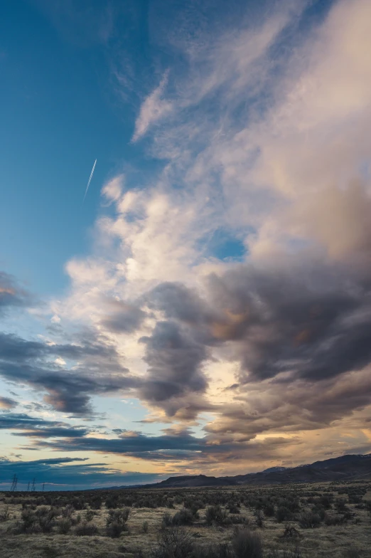 a plane flying through a cloudy sky over a desert, by Neil Blevins, cinematic shot ar 9:16 -n 6 -g, sunset clouds, long