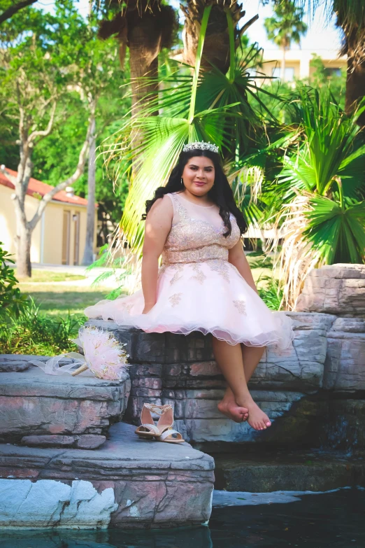 a woman in a pink dress sitting on a rock wall, by reyna rochin, posing as a queen, 1 6 years old, plus size, slightly pixelated