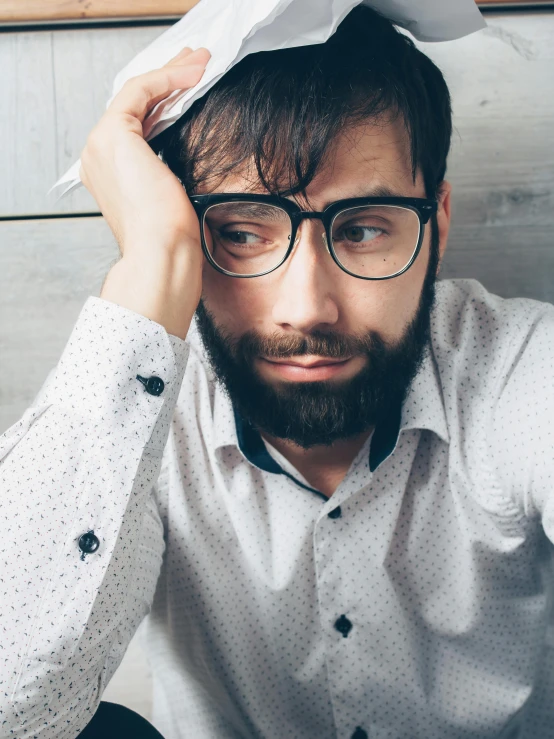 a man with a paper hat on his head, inspired by Nelson Alexander Ross, trending on pexels, square rimmed glasses, short scruffy beard, looking exhausted, androgynous male