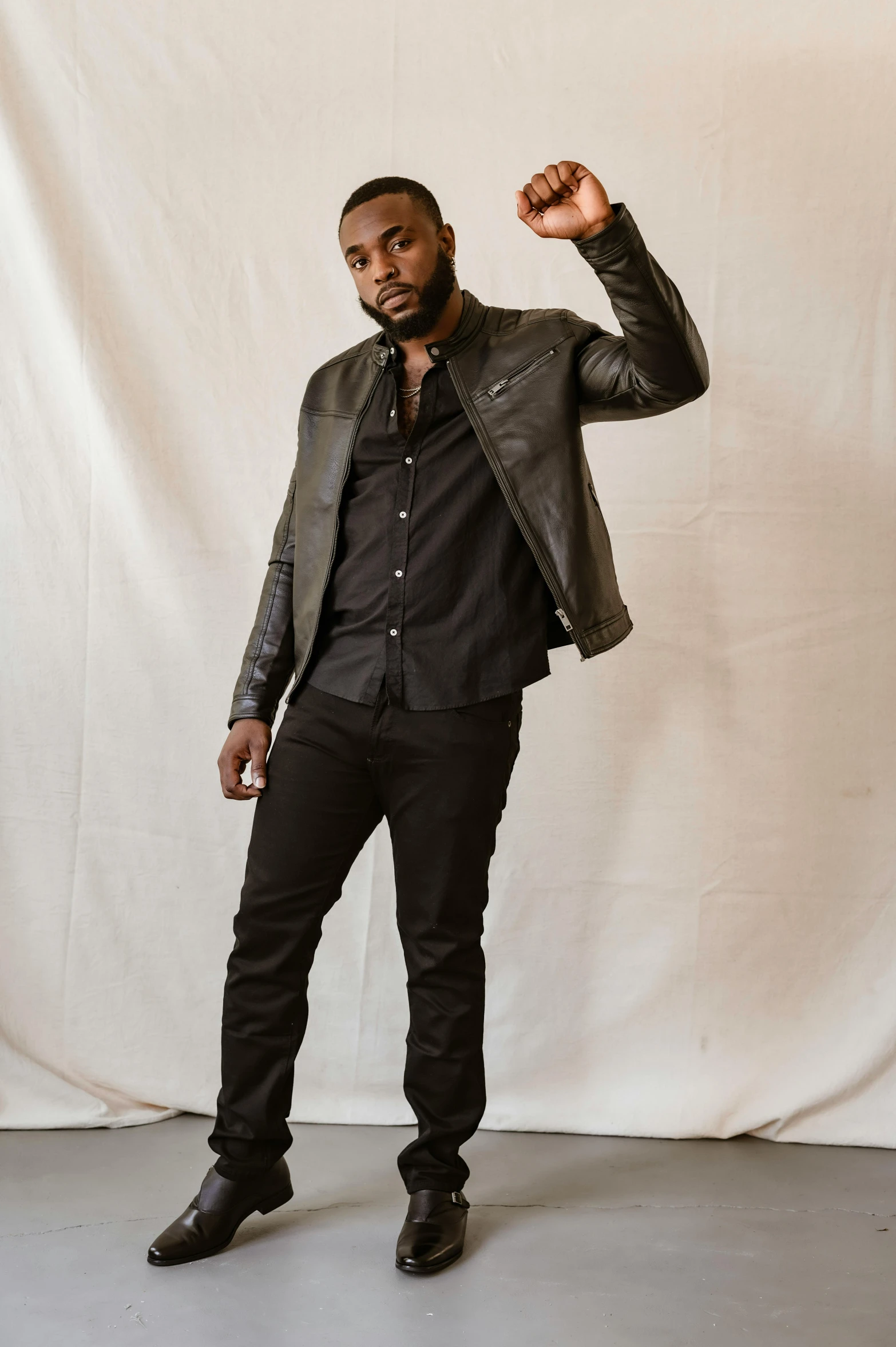 a man standing in front of a white backdrop, inspired by Theo Constanté, pexels contest winner, black arts movement, wearing a leather jacket, matte black pants, jaylen brown, wearing black grey suit