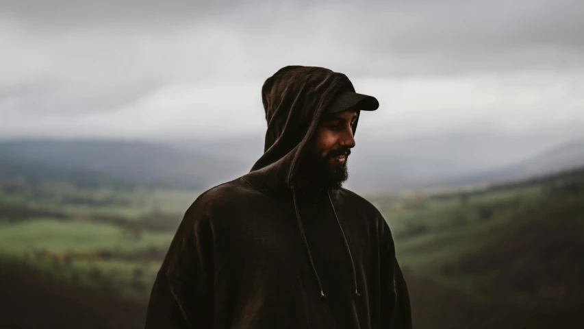 a man with a beard wearing a hoodie, an album cover, pexels contest winner, overlooking a valley, overcast lighting, wearing dark cloak, profile pic