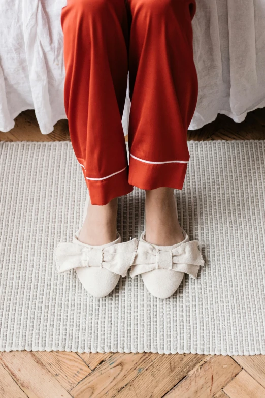 a woman sitting on a bed wearing red pants and white shoes, thick bow, ivory rococo, full product shot, slippers