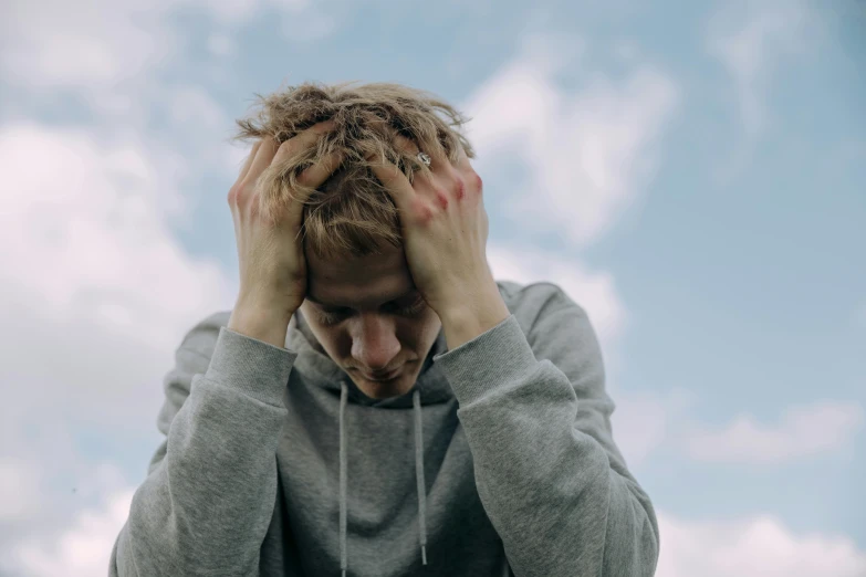 a man holding his head in his hands, a picture, pexels, sad sky, messy blond hair, thin young male, recovering from pain