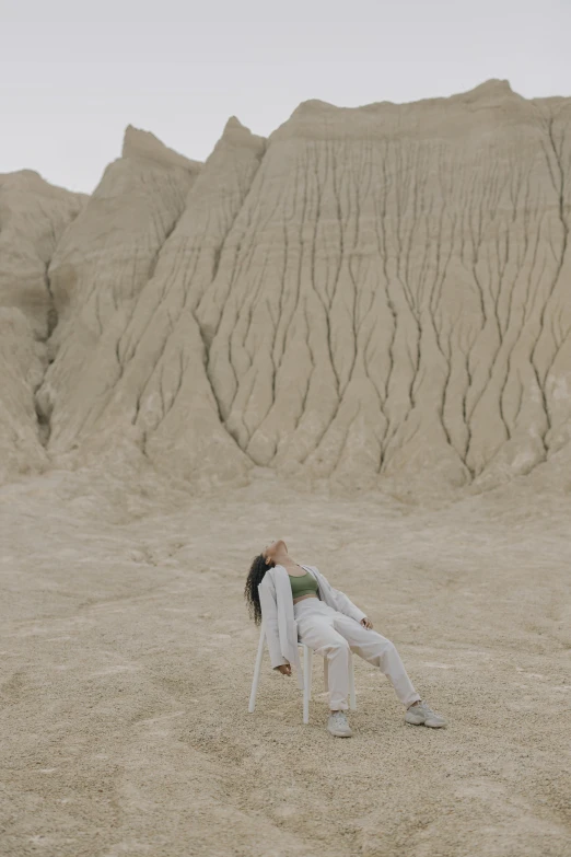 a woman sitting on a chair in a desert, by Attila Meszlenyi, unsplash contest winner, surrealism, white clay, badlands, face down, geology