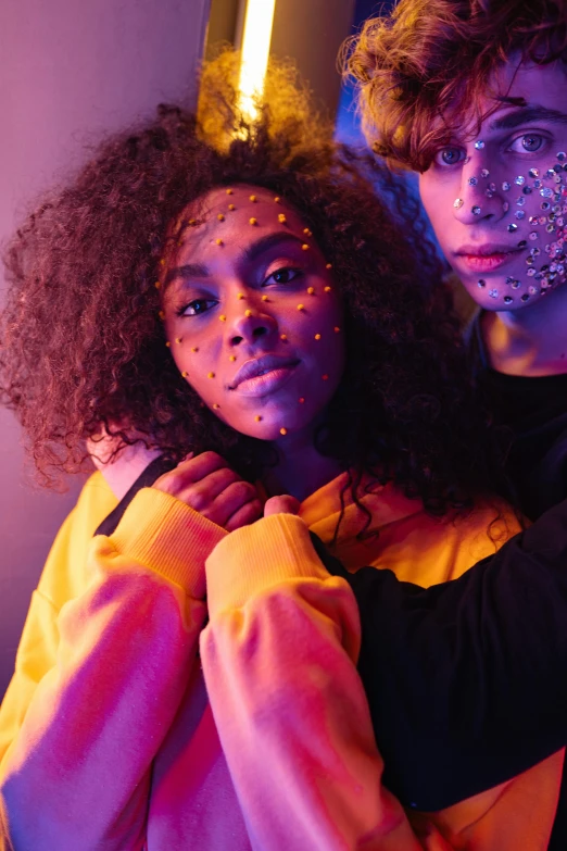 a man and a woman standing next to each other, trending on pexels, afrofuturism, glowing yellow face, lesbians, glitter, teenage girl