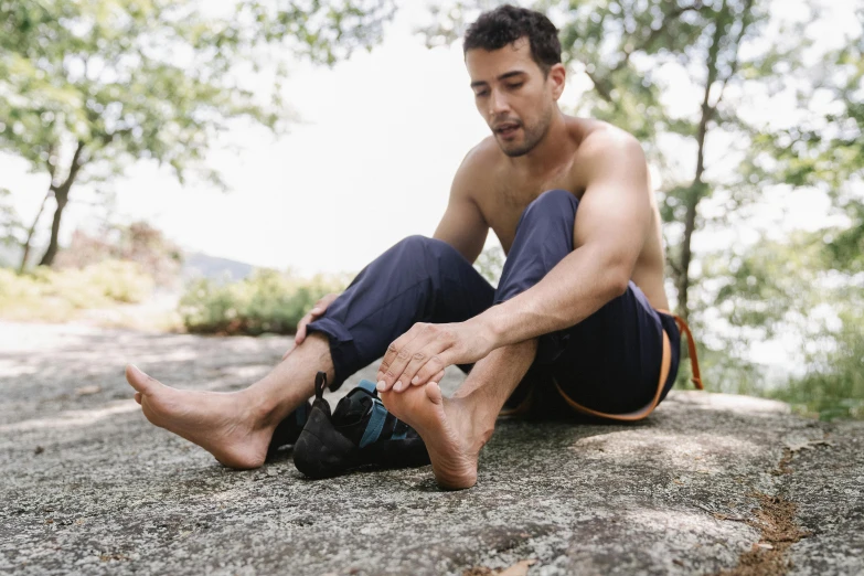 a shirtless man sitting on top of a rock, by Meredith Dillman, unsplash, foot wraps, with wires and bandages, avatar image, manly