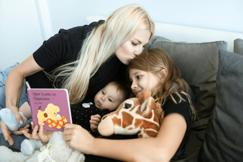 a woman reading a book to two children, pexels contest winner, sofie the giraffe, blue'snappy gifts'plush doll, blonde, eye level view