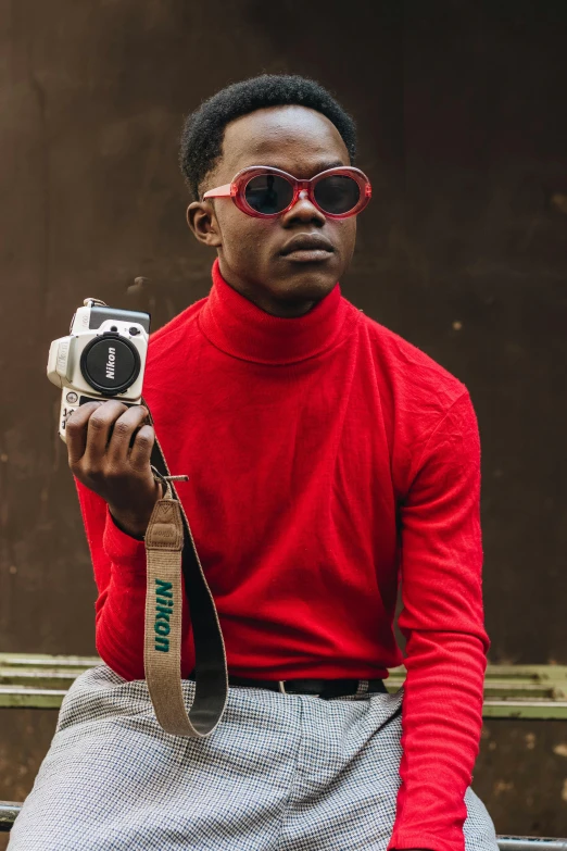 a man in a red shirt is holding a camera, an album cover, inspired by David Bailly, trending on pexels, hi mark ( akwaaba tommy ), fashion shoot, wearing turtleneck, vintage colours