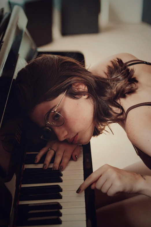 a woman laying on the floor next to a piano, inspired by Elsa Bleda, trending on pexels, girl with glasses, eyes closed, mellotron, laetitia casta