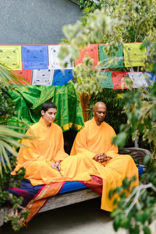 a couple of people that are sitting on a bench, yellow robes, in a jungle environment, meditating, vibrant greenery