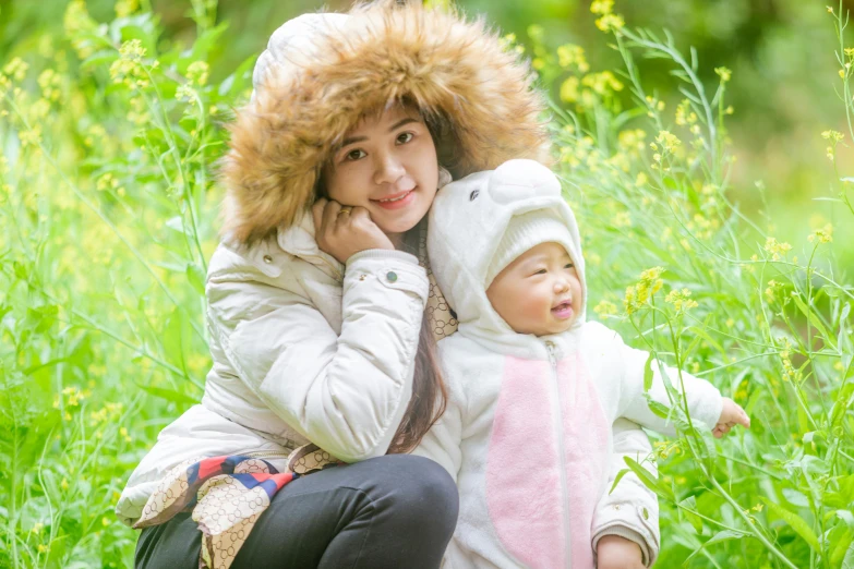 a woman sitting next to a baby in a field, a picture, fur hood, hangzhou, portrait image