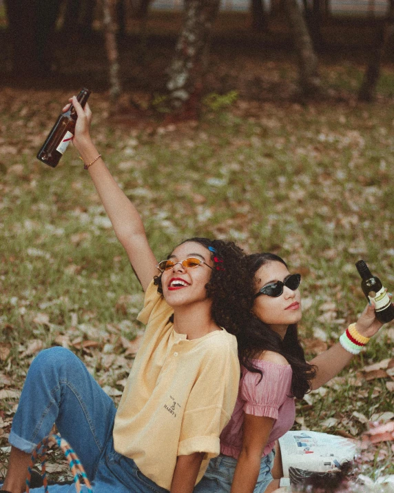 a couple of women sitting on top of a grass covered field, a picture, trending on pexels, happening, holding a bottle of beer, shades, ashteroth, pictured from the shoulders up