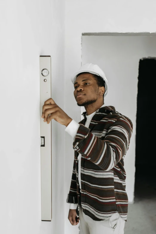 a man that is standing in a room with a ruler, by Everett Warner, pexels contest winner, leaning on door, afro tech, concerned, ignant