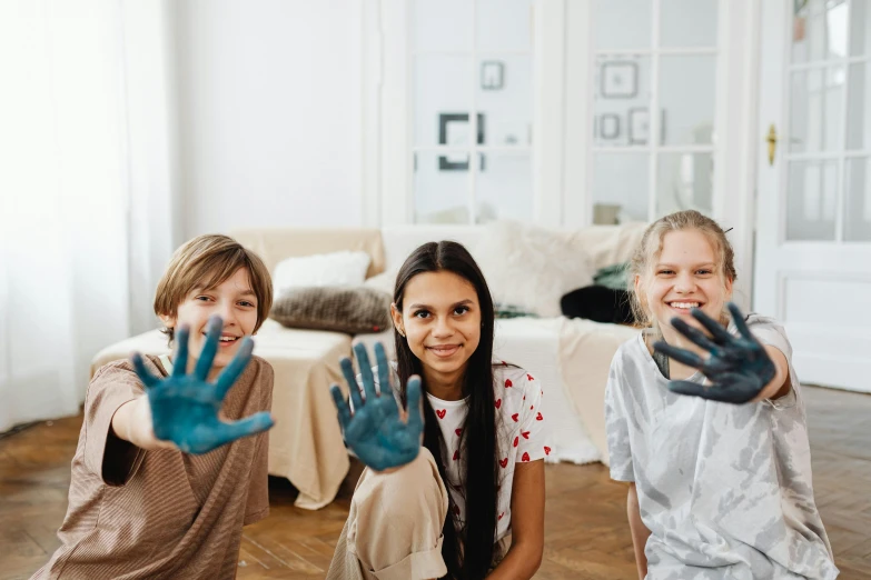 three girls sitting on the floor with their hands painted, pexels contest winner, action painting, wave a hand at the camera, blue and gray colors, at home, teen boy