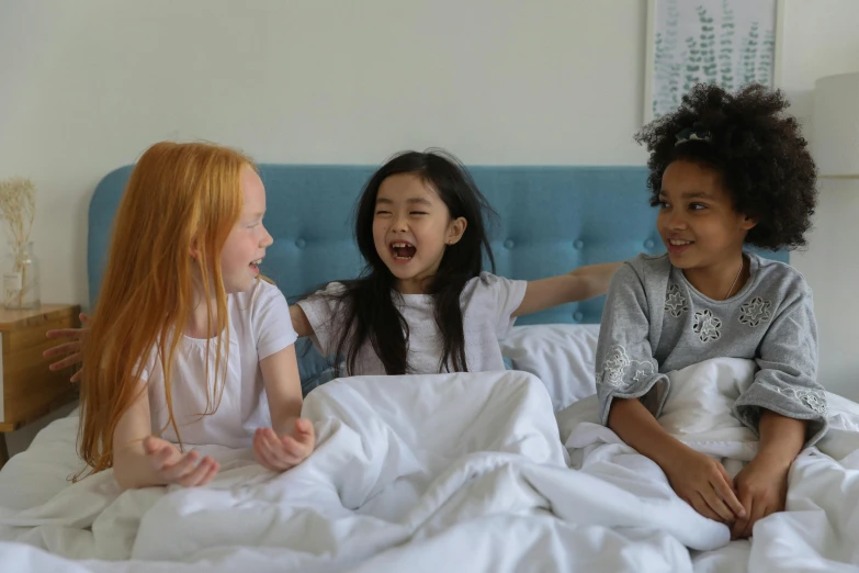 a group of young girls sitting on top of a bed, laughing, white sheets, bixbite, easy to use