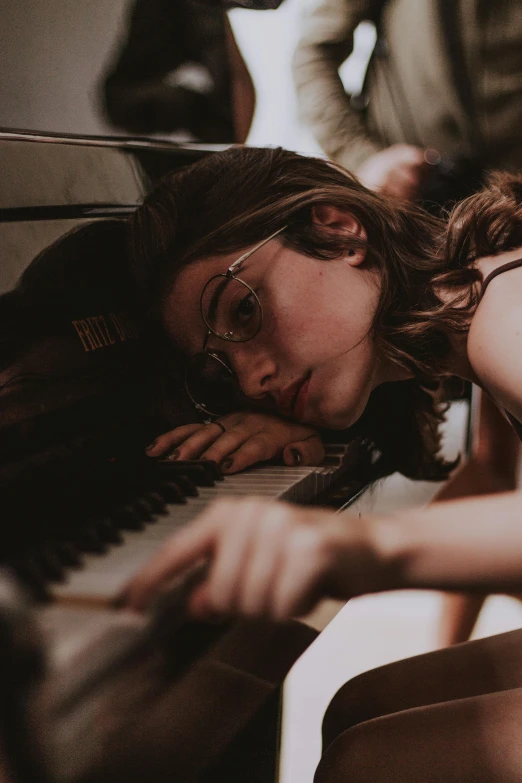 a woman laying on top of a couch next to a piano, inspired by Elsa Bleda, trending on pexels, girl with glasses, girl with brown hair, profile image, performing