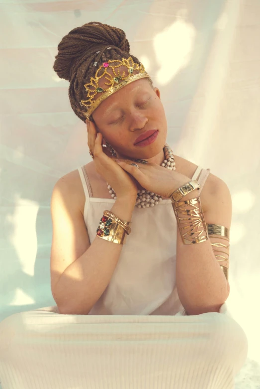 a woman sitting in a bath tub with her hands on her face, an album cover, inspired by Makoto Aida, unsplash, afrofuturism, albino, with a gold crown, in a white boho style studio, brass bracelets