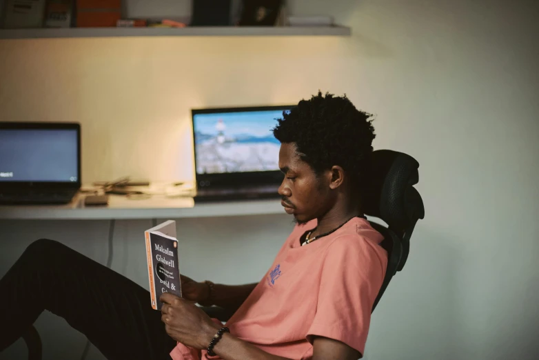 a man sitting in a chair reading a book, by Barthélemy Menn, pexels contest winner, afrofuturism, home office, programming, ignant, jayison devadas